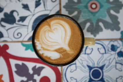 Cup of MannaBrew with latte art against a patterned tile background