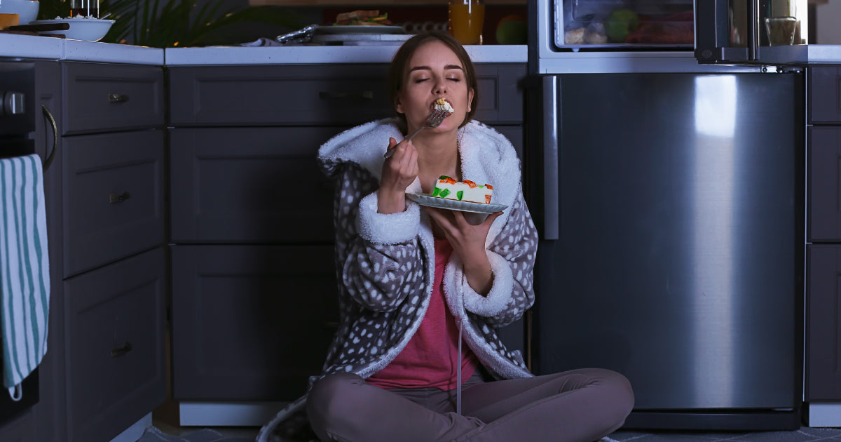 A woman snacking in front of her fridge