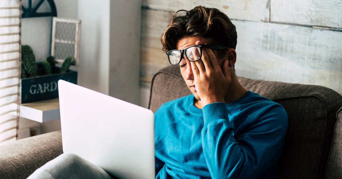 Person rubbing their eyes, behind their laptop, tired