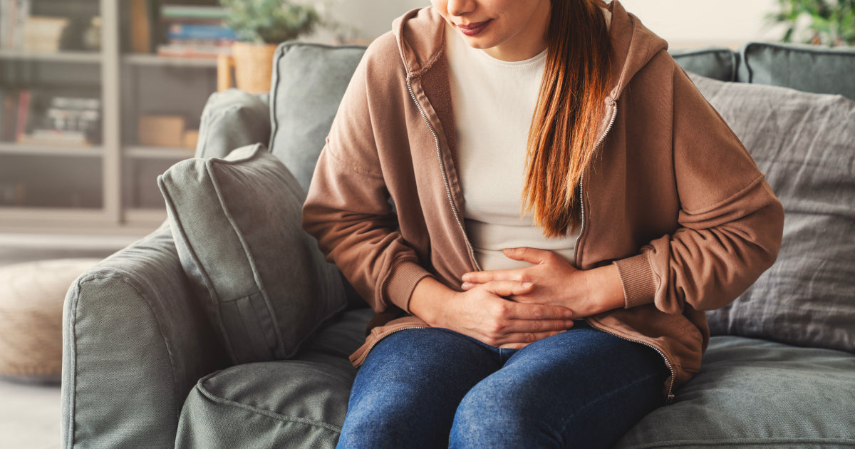 woman holding stomach, sitting on a couchj