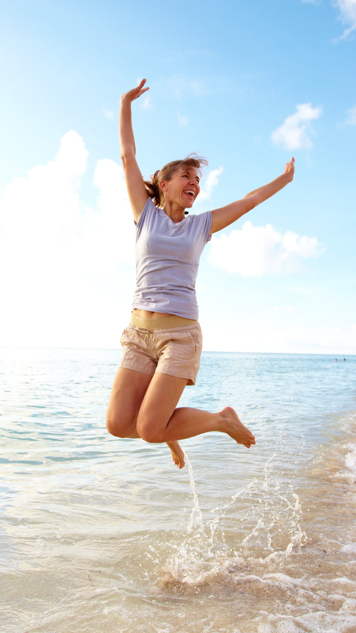Woman jumping joyfully on a beach with clear blue sky and ocean.