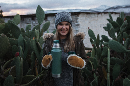 Person holding a thermos of MannaBrew in front of cacti