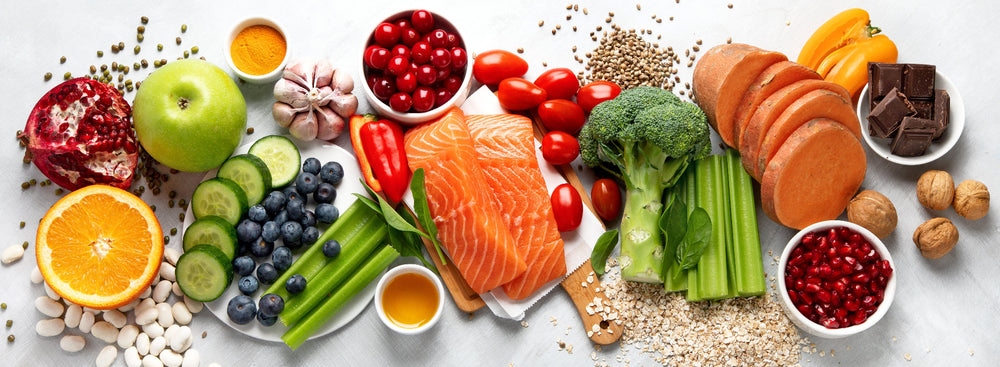 Assorted healthy foods including fruits, vegetables, and salmon on a white background