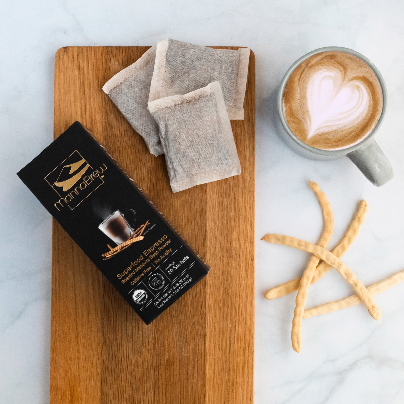 MannaBrew 20 Sachet on a wooden board with mesquite pods and a latte